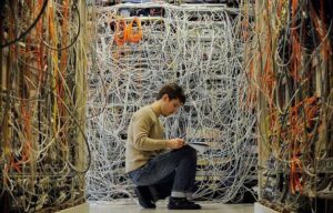 A man with a pad and pencil surrounded by tons of crossed wires